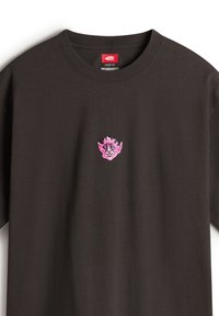 Camiseta negra de corte holgado hecha de algodón, con un pequeño gráfico rosa de una cara con cuernos en el pecho, escote redondo.