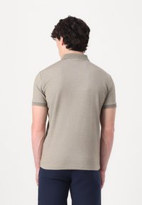 Khaki polo majica z teksturirano tkanino, kratkimi rokavi in ovratnikom. Ima subtilen vzorec in kontrastni rob pri ovratniku.
