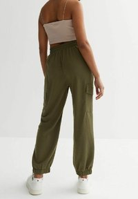 Olive’owe zielone spodnie cargo z elastycznymi mankietami, posiadające dwie boczne kieszenie, wykonane z lekkiego materiału. Noszone z beżowym topem typu crop.