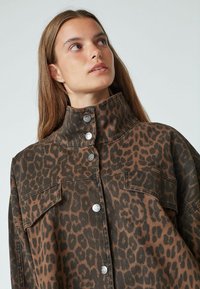 Leopard print shirt jacket in brown and black. Features a high collar, large front pockets, and silver snap buttons. Soft textured material.