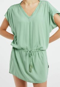 Robe verte à manches courtes en V, fabriquée dans un matériau doux, avec une taille à cordon de serrage à pompons et une coupe décontractée.