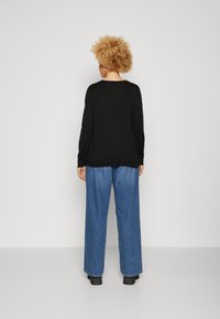 Black long-sleeve sweater with a relaxed fit, paired with light blue wide-leg jeans and black footwear. Texture appears soft and casual.