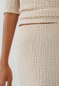 Beige strukturierter Stofftop und -rock mit Raffung. Nahaufnahme, die die weiche, zerknitterte Oberfläche und die elastische Raffung am Bund zeigt.