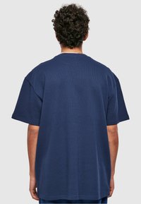 Sötétkék, oversized póló, texturált anyagból készült, kerek nyakkal és rövid ujjakkal, hátulról látható.