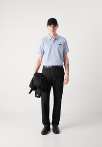 Polo shirt bleu clair, pantalons en jean noir, ceinture noire et chaussures noires. Tient une veste noire. Présente un logo sur le col du polo.