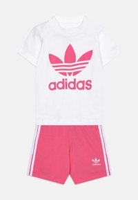 White cotton t-shirt with large pink Adidas logo; pink shorts with white side stripes and logo on the hem.