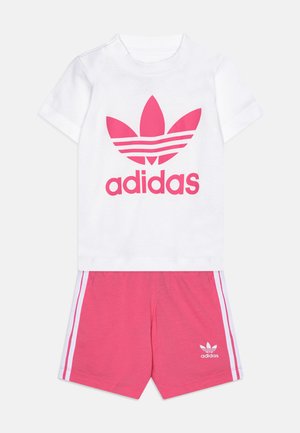 T-shirt bianco in cotone con grande logo Adidas rosa; pantaloni corti rosa con strisce bianche ai lati e logo sull'orlo.