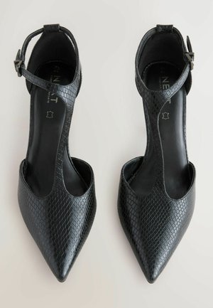 Zapatos de tacón negros con puntera afilada, que presentan un patrón texturizado y una correa en el tobillo. El interior tiene un acabado suave.