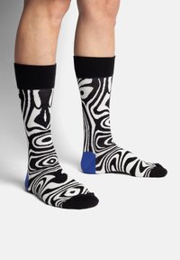 Schwarz-weiß gemusterte Socken mit blauen Akzenten an den Fersen, die ein abstraktes, wirbelndes Design und einen gerippten schwarzen Saum aufweisen.
