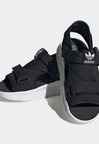 Black Adidas sandals with open toes, adjustable straps, mesh fabric, and thick white soles on a plain light background.