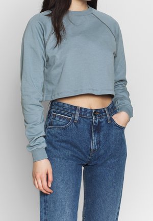 Top corto de manga larga azul claro con cuello redondo y puños acanalados, combinado con vaqueros de denim oscuro de cintura alta.