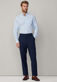 Lichtblauwe overhemdd met verticale witte strepen, gecombineerd met donkerblauwe broek en bruine instapschoenen. Eenvoudige kraag en slim fit ontwerp.