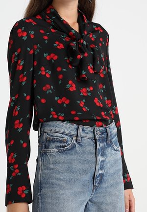 Blusa nera con motivo floreale rosso, con scollo annodato. Abbinata a jeans chiari, strappati e a vita alta.