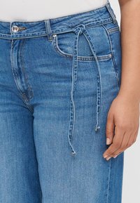 Light blue denim pants with a relaxed fit, featuring a drawstring tie at the waist, front pockets, and a subtle faded texture.