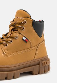 Stivaletto in suede marrone con accenti neri, punta rotonda, lacci in tessuto, logo del marchio e suola in gomma testurizzata con battistrada profondo.