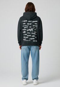 Felpa nera con testo bianco in varie lingue tra cui "AMORE", abbinata a jeans azzurri larghi e sneakers bianche.