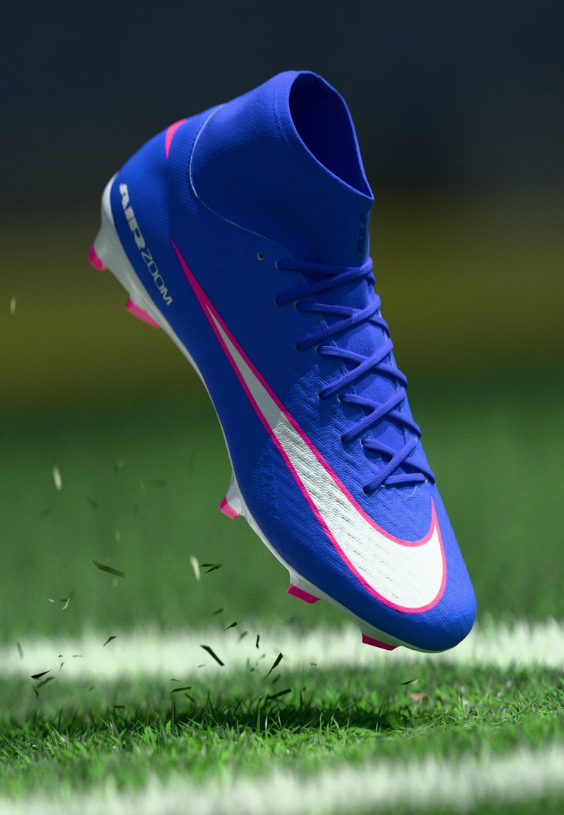 Μπλε ποδοσφαιρικό παπούτσι Nike με ψηλή σχεδίαση, λευκές και ροζ λεπτομέρειες, υφή επιφάνειας και ροζ στήριγματα, σε φόντο πράσινης χλόης.