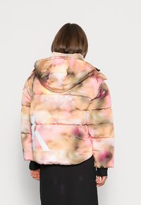 Giubbotto imbottito in rosa pastello e beige con motivo floreale astratto. Presenta un cappuccio, polsini elasticizzati e un logo stampato sulla schiena.
