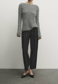 Grauer und weißer Strickpullover mit langen Ärmeln, kombiniert mit schwarzen Hosen. Schmale, gerade geschnittene Hosen mit glatter Textur und minimalistisches Design.