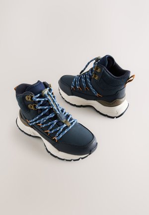 Marineblauwe wandelschoenen met een gestructureerd bovenwerk, blauwe veters en metalen oogjes. Voorzien van een dikke witte zool en een gevoerde kraag voor comfort.