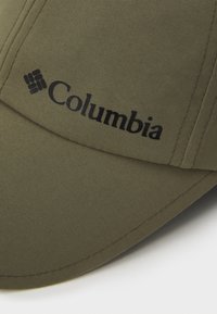 Oliwkowa czapka baseballowa z materiału, z czarnym logo "Columbia" i widocznymi detalami ściegów na daszku i panelach.