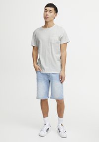 Tricou gri cu pete, având buzunar, purtat cu pantaloni scurți din denim de un albastru deschis. Asortat cu adidași albi și șosete albe până la glezne. Ținută simplă și casual.