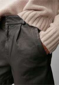 Černé kožené kraťasy s záhyby, nošené pod světle růžovým žebrovaným svetrem. Kůže má hladkou strukturu a přiléhavý střih.