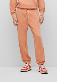 Helle orange Sweatpants mit Kordelzugbund, elastischen Bündchen und Seitentaschen, kombiniert mit rot-weißen Sneakers mit schwarzen Akzenten.