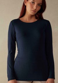 Marineblaues Langarmshirt, taillierte Passform, runder Halsausschnitt, aus weichem, dehnbarem Stoff mit glatter Textur und dezentem Glanz.