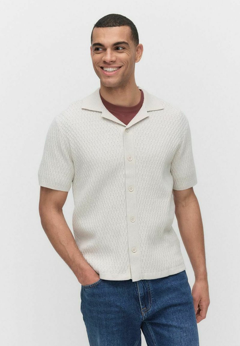 Korte mouwen, crèmekleurig gebreid shirt met een gestructureerd patroon, knoopsluiting aan de voorkant en een casual kraag, gecombineerd met blauwe denim jeans.