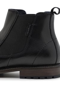 Botín negro de cuero con paneles laterales elásticos, resistente tacón de madera marrón y costuras visibles en la parte superior.