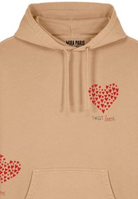 Bež hooded dukserica s prednjim džepom. Na prednjoj strani se nalazi crvena grafika srca sastavljena od manjih srca i tekst "SWEET heart" u crnoj boji.