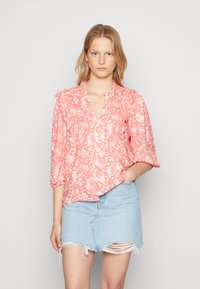 Blusa floral rosa com mangas bufantes, decote em V e padrões de flores brancas, combinada com uma saia de ganga clara com bainha desfiada.