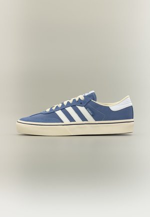 Baskets Adidas Samba bleues avec des bandes blanches, des lacets et une semelle blanches, présentées en profil latéral sur un fond neutre.