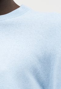 Pull bleu clair en maille avec un col rond. La texture est douce et légèrement côtelée, mettant en valeur une surface lisse et uniforme.