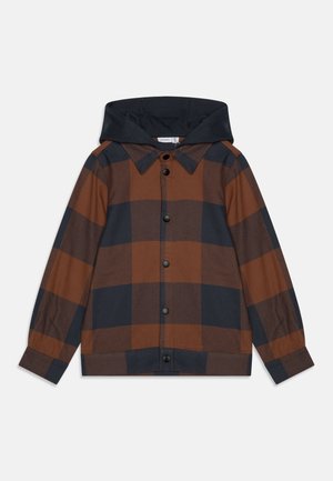 Chaqueta grande con capucha y cuadros grandes marrón y negro, con cierre de presión y mangas largas, extendida sobre un fondo blanco.