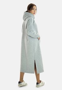 Vestido sudadera gris de gran tamaño con mangas largas, bolsillos laterales y una abertura en la parte posterior. Hecho de un tejido suave, presenta una capucha amplia y un corte holgado.