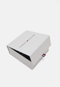 Hvit Tommy Hilfiger-boks med merkevarelogo på toppen, noe åpen, som viser et svart-hvittstripet plagg inni.