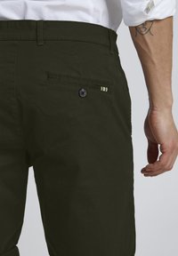 Pantalons vert foncé en tissu doux, dotés d'une seule poche arrière avec un bouton et un accent rayé.