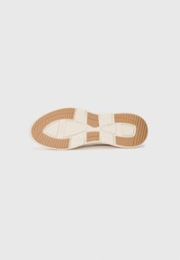Shoe outsole with a textured design, combining cream and brown colors. Features grooves for traction and a rounded toe shape.