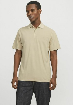 Polo shirt beige de tela suave, con un cuello clásico, mangas cortas, una botonera de tres botones y un logo bordado en el pecho.