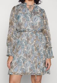 Vestido de estampado paisley con mangas largas elásticas, cierre de cuello con lazo y cintura fruncida. El material parece ligero y fluido.