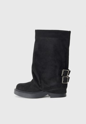 Zwarte kniehoge laarzen van suede met een gladde textuur. Voorzien van twee zilveren gespen aan de zijkant en een dikke zwarte zool.