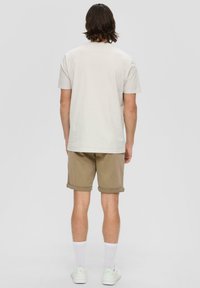 Hellgraues T-Shirt mit kurzen Ärmeln, kombiniert mit hochgekrempelten khakifarbenen Shorts, getragen mit weißen Socken und hellgrünen Turnschuhen. Einfaches Design.