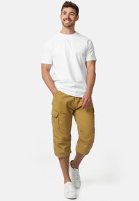 T-shirt blanc en coton associé à un short cargo kaki de longueur genou, doté de poches latérales, d'ourlets retroussés et de baskets blanches.