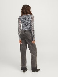 Μακρυμάνικη μπλούζα σε διαφανές μαύρο και λευκό ζε�βρέ ζωγραφιστή μνήμης, σε συνδυασμό με ψηλόμεσα σκούρα γκρι παντελόνια σε φαρδιά γραμμή με διπλωμένα μπατζάκια και τσέπες.