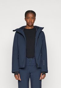 Chaqueta aislante de color azul marino con cremallera frontal, gran capucha y puños ajustables. Presenta una textura suave con un diseño de marca mínimo y bolsillos con cremallera.