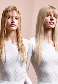 Två modeller med olika frisyrer: en har långt, blött, rakt hår medan den andra har slätt, rakt, ljust blont hår. Båda bär vita ribbade toppar.