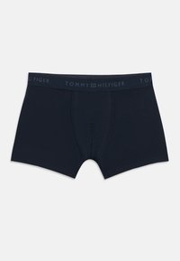 Polkavske moške boksarice temno modre barve s šivi in elastičnim pasom z logotipom Tommy Hilfiger na belem ozadju.