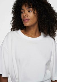 Witte oversized t-shirt met een ronde halslijn en korte mouwen. Kenmerkt zich door een subtiel reliëfontwerp in lichtbeige over de borst.